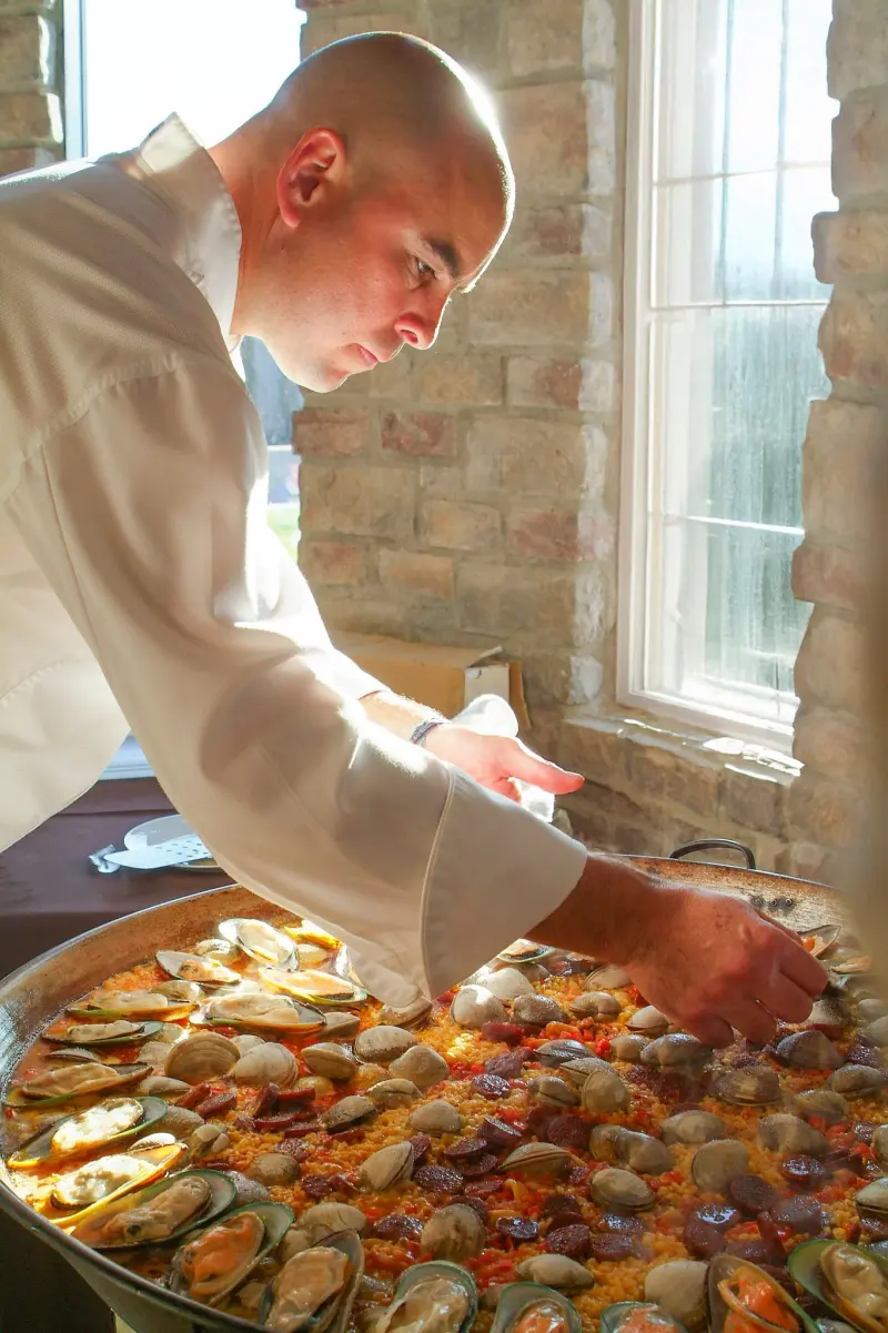 Chef finishing a large pan of seafood paella at a restaurant event