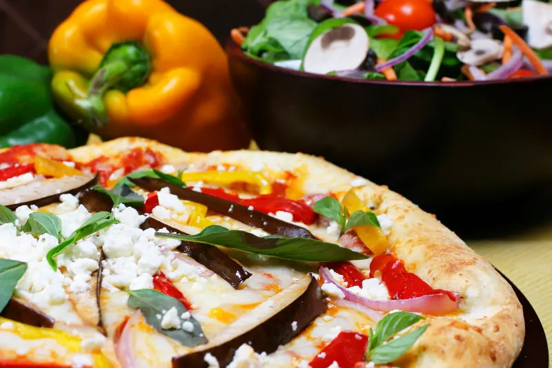 Rustic pizza with roasted eggplant, peppers, feta and fresh basil beside a garden salad