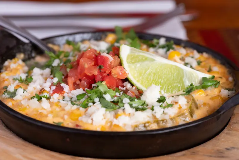 Mexican street corn esquites in a cast-iron skillet with cotija, pico de gallo and lime