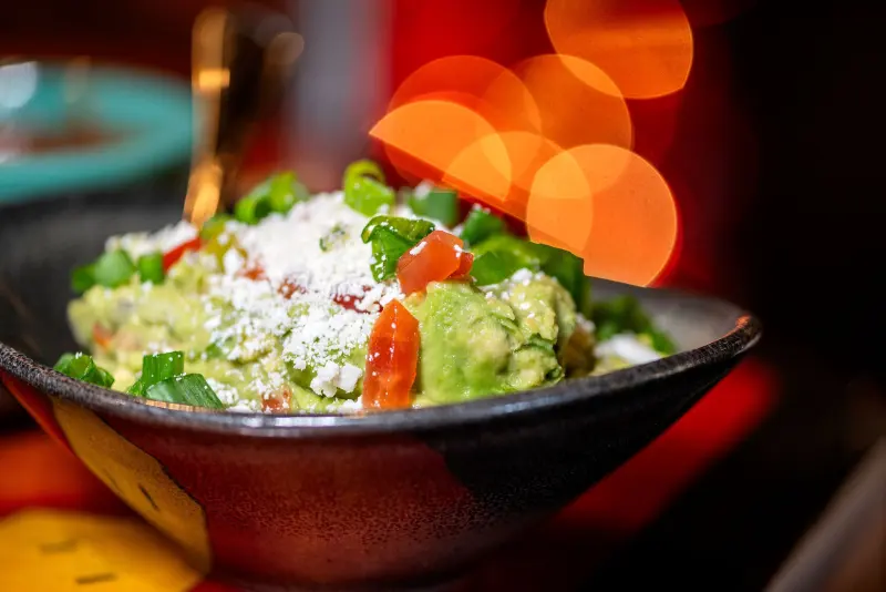 Guacamole with queso fresco and tomato against warm restaurant lights