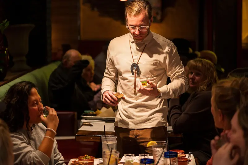 Server presenting dishes tableside to guests in a busy restaurant dining room