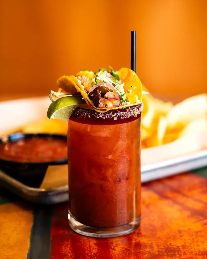 Michelada-style cocktail garnished with a street taco and lime