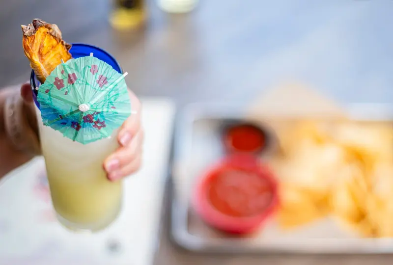 Tropical cocktail with paper umbrella, chips and salsa in the background