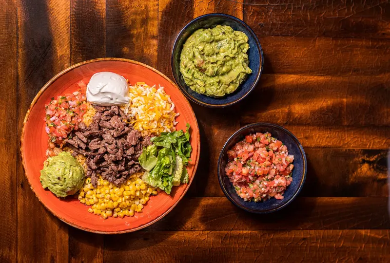 Overhead of a carne asada plate with corn, pico de gallo, guacamole and salsa